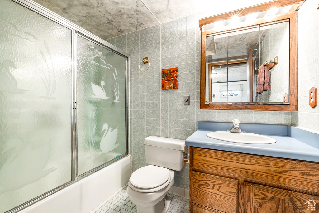Bathroom with tile walls, vanity, tile patterned flooring, shower / bath combination with glass door, and toilet