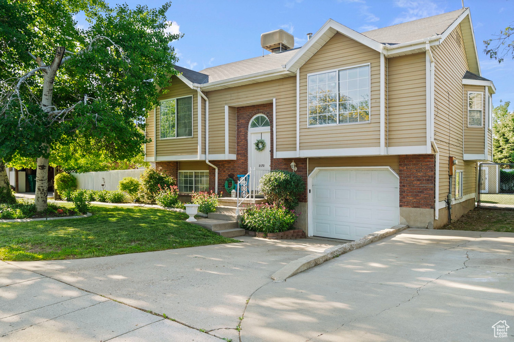 Split foyer home featuring driveway, brick siding, and a garage