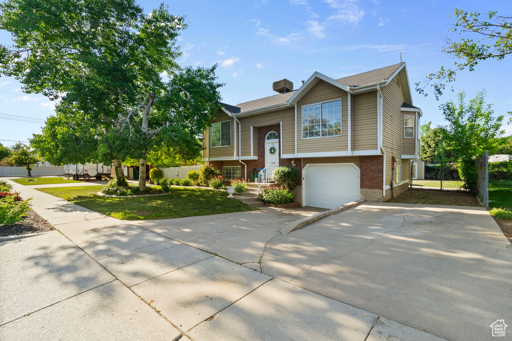 Raised ranch with concrete driveway, a garage, brick siding, and a front yard