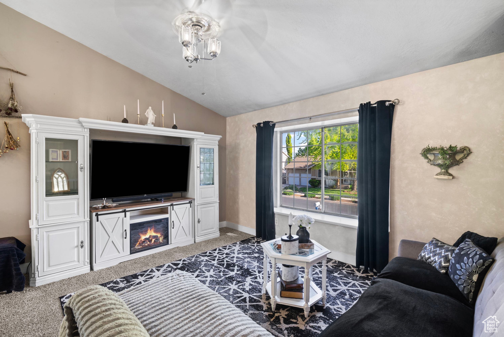Living room featuring lofted ceiling, carpet flooring, a lit fireplace, ceiling fan, and baseboards