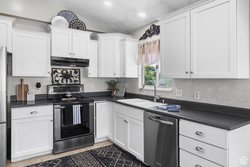 Kitchen featuring appliances with stainless steel finishes, a sink, under cabinet range hood, dark countertops, and white cabinets