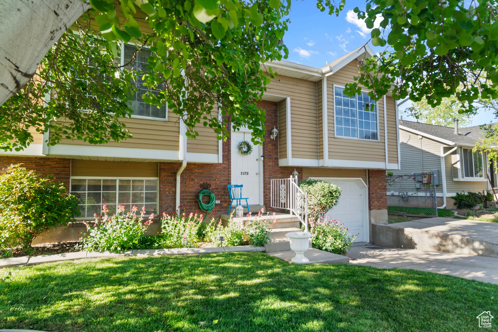 View of front facade featuring brick siding, a garage, a front lawn, and concrete driveway
