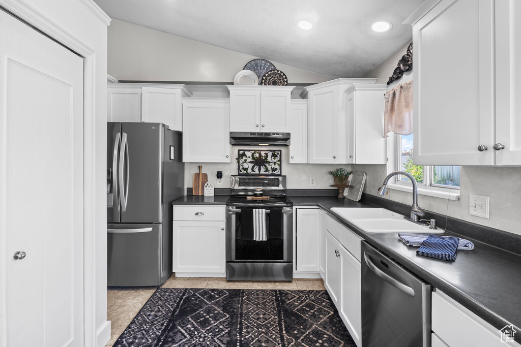 Kitchen with stainless steel appliances, under cabinet range hood, lofted ceiling, a sink, and white cabinetry