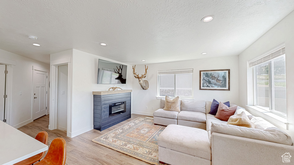 Living area featuring light wood-style flooring, a textured ceiling, recessed lighting, baseboards, and a glass covered fireplace