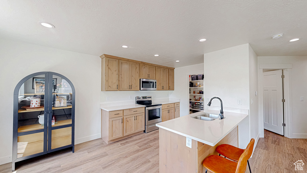Kitchen with appliances with stainless steel finishes, a sink, light wood-type flooring, light brown cabinets, and a kitchen breakfast bar