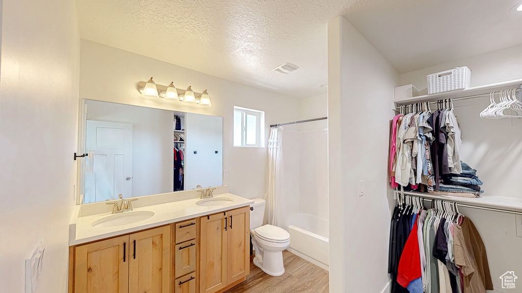 Full bath with wood finished floors, double vanity, a walk in closet, toilet, and shower / tub combo