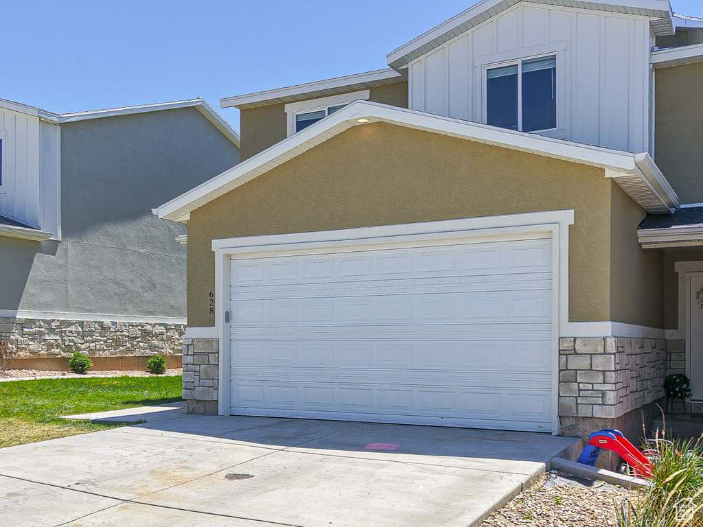 Townhome / multi-family property with stone siding, a garage, board and batten siding, and concrete driveway