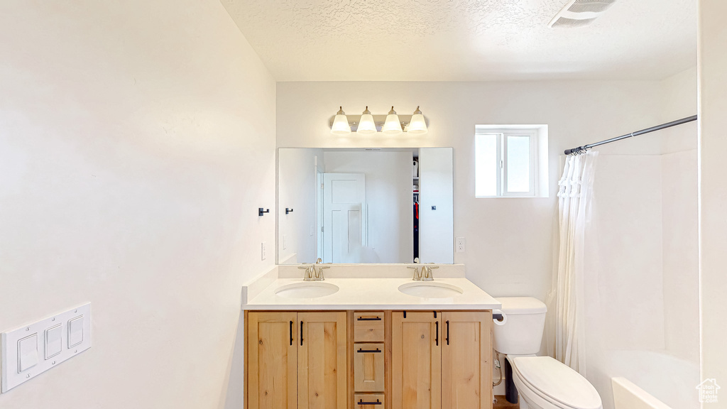 Full bath with toilet, double vanity, and a textured ceiling