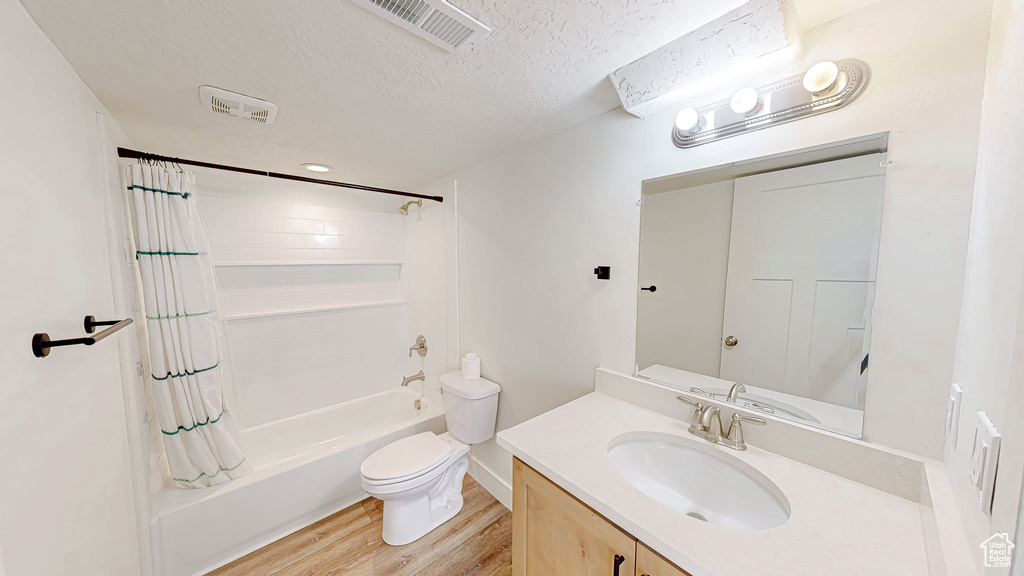Full bathroom featuring wood finished floors, a textured ceiling, toilet, shower / bath combo, and vanity
