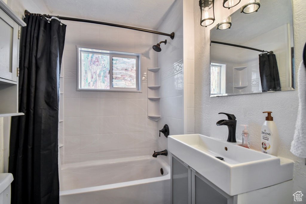 Bathroom featuring shower / bath combination with curtain, vanity, toilet, and a textured wall