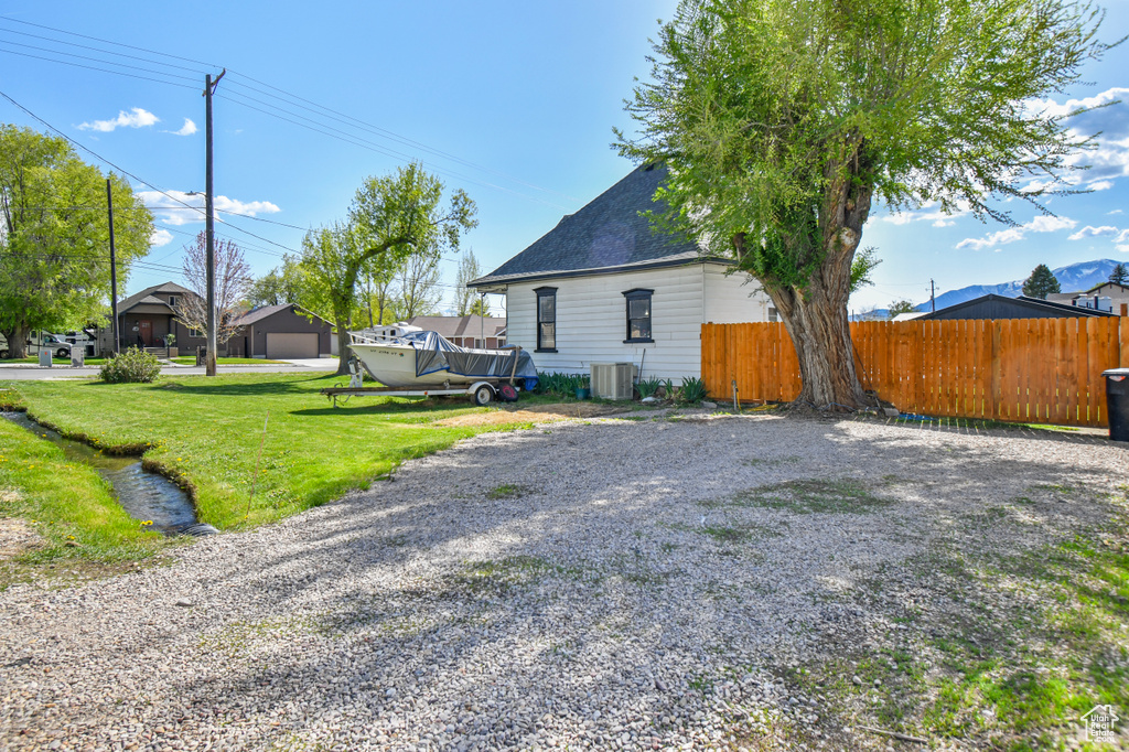 View of side of property featuring central air condition unit, a detached garage, and gravel driveway