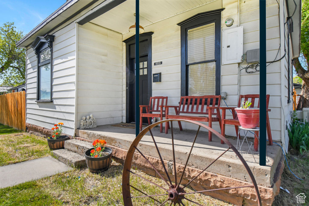Doorway to property with covered porch, electric panel, and fence