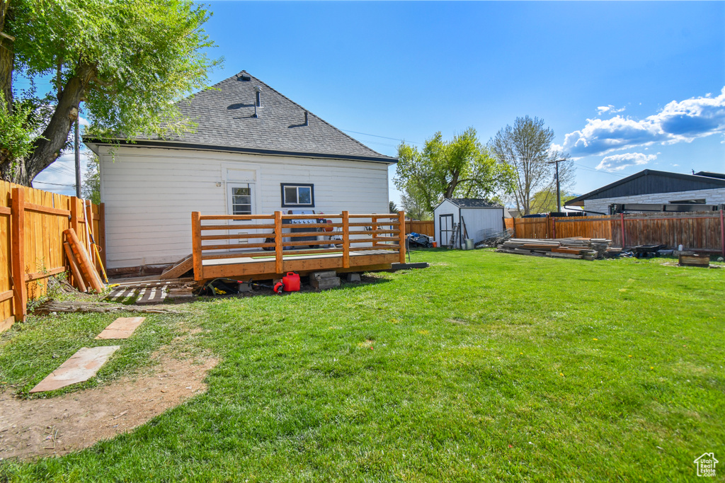 Back of house with a deck, a shed, an outbuilding, and roof with shingles