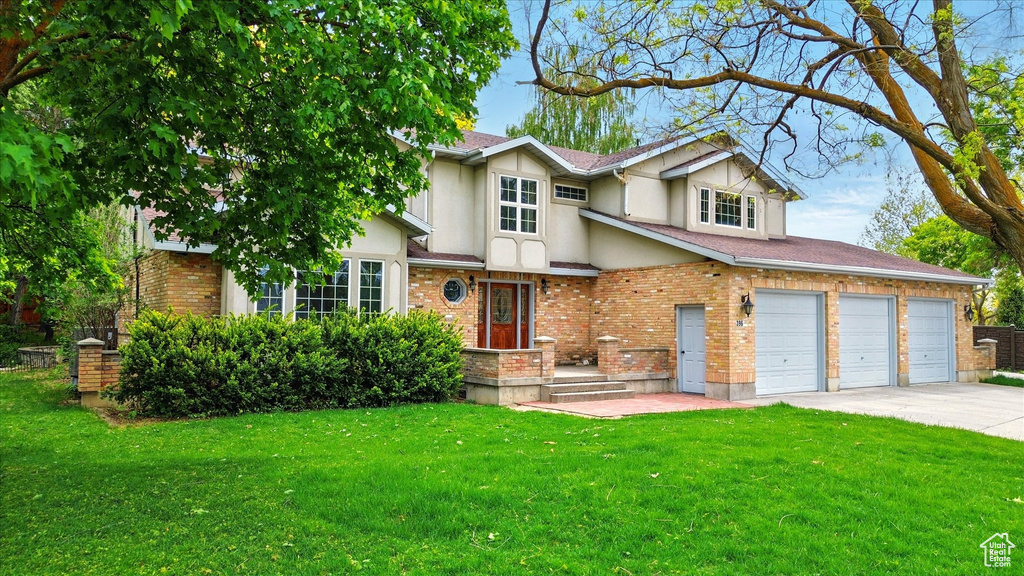 View of front of house with a front lawn, driveway, stucco siding, and brick siding
