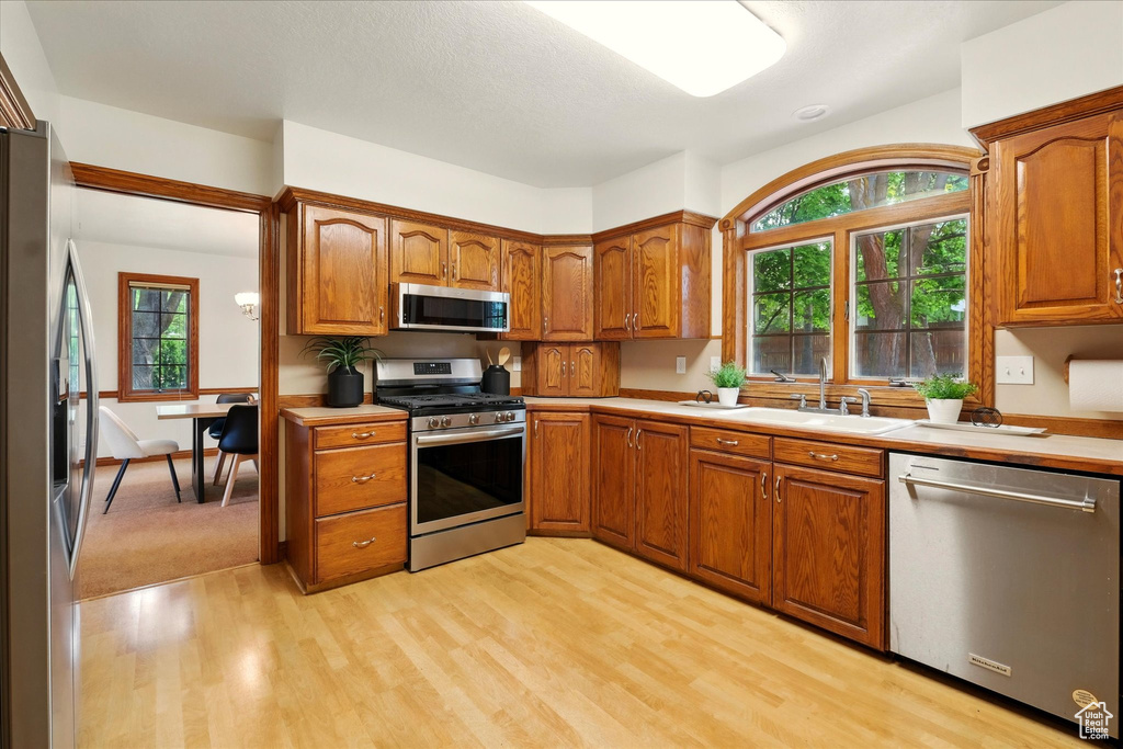 Kitchen featuring stainless steel appliances, light wood-type flooring, brown cabinets, and a sink
