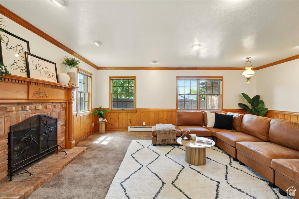 Carpeted living room with a wainscoted wall, baseboard heating, wooden walls, a brick fireplace, and ornamental molding