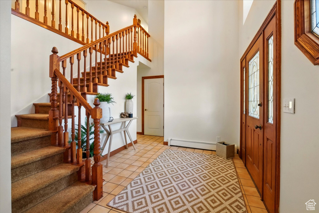 Foyer featuring baseboard heating, a high ceiling, light tile patterned floors, stairs, and baseboards