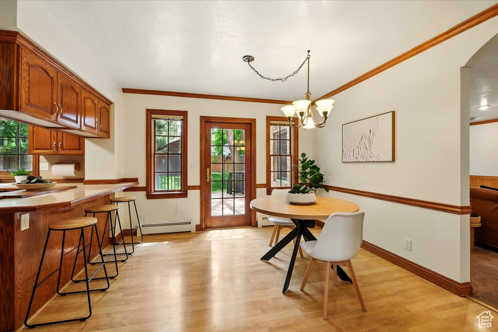 Dining space with light wood finished floors, a chandelier, baseboard heating, baseboards, and crown molding