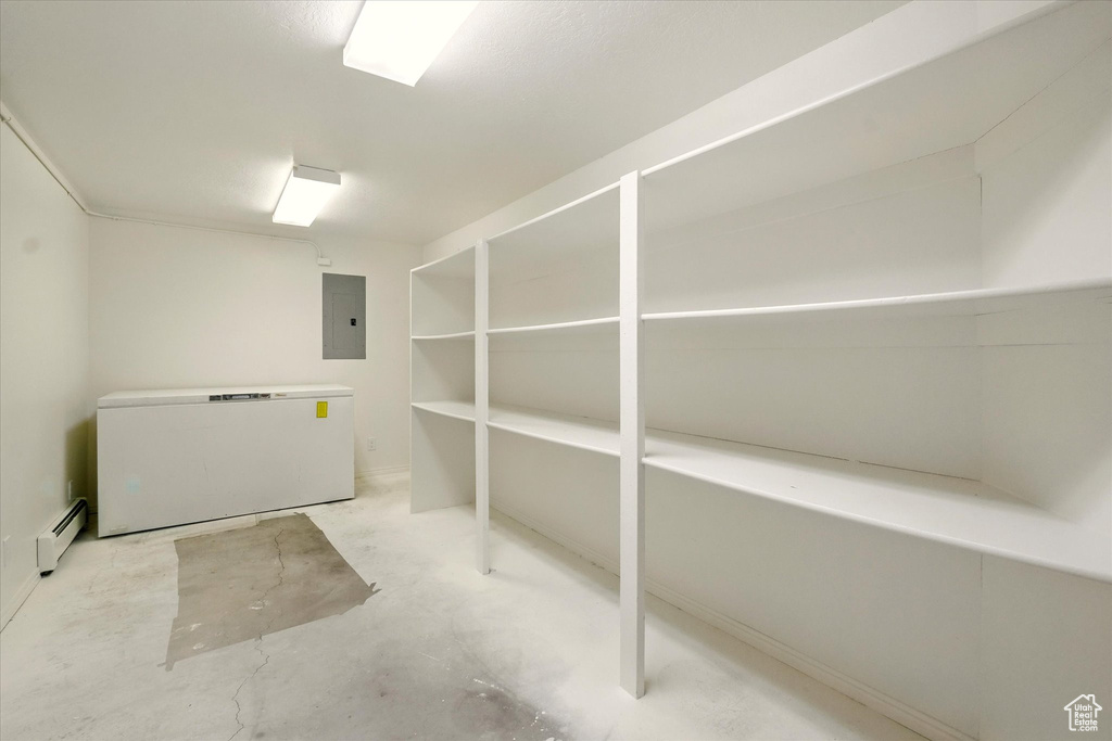 Below grade area featuring fridge, electric panel, and baseboard heating