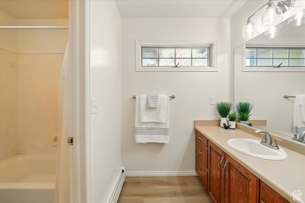 Full bath with wood finished floors, vanity, a baseboard heating unit, baseboards, and shower / bath combo with shower curtain