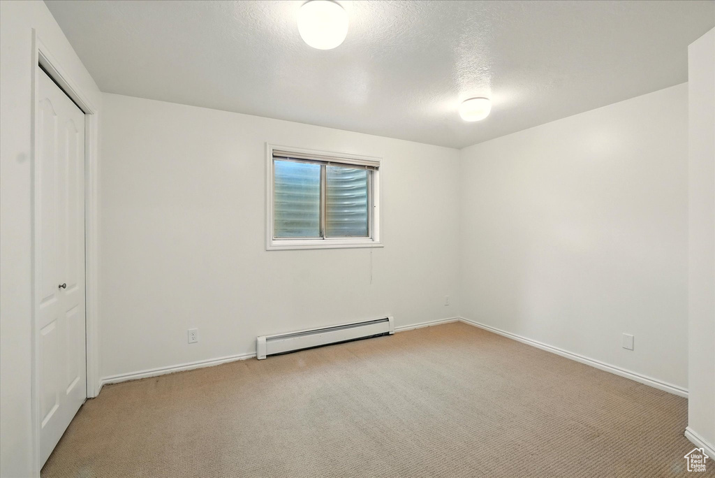 Unfurnished bedroom with baseboard heating, light carpet, baseboards, a closet, and a textured ceiling