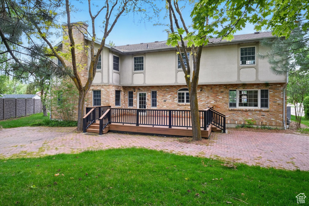 Rear view of house with stucco siding, a chimney, a deck, and brick siding