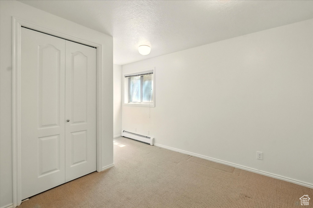 Unfurnished bedroom featuring a baseboard heating unit, light carpet, a closet, baseboards, and a textured ceiling