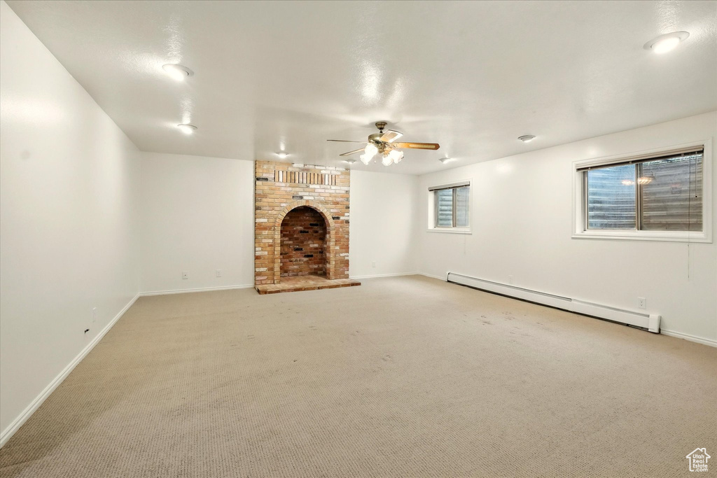 Unfurnished living room with a baseboard heating unit, a fireplace, ceiling fan, baseboards, and light colored carpet