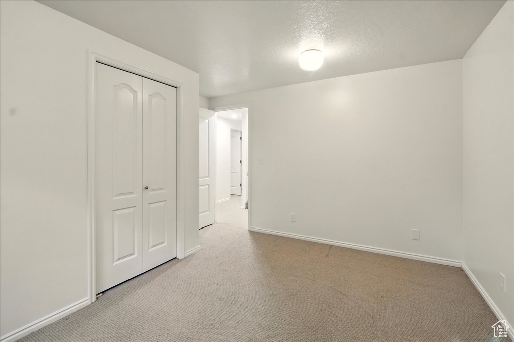 Unfurnished bedroom with light carpet, baseboards, and a closet