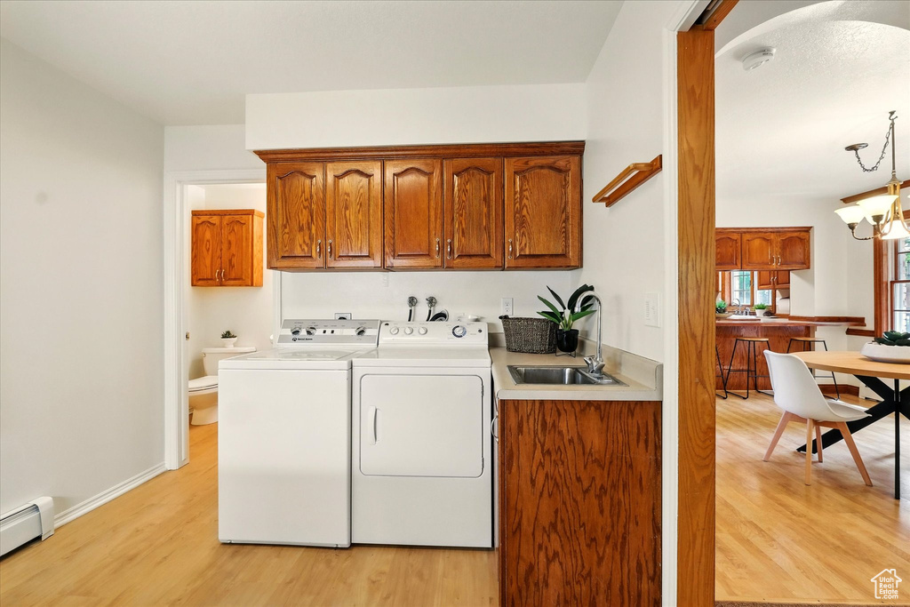 Clothes washing area with cabinet space, separate washer and dryer, light wood-type flooring, and a baseboard radiator
