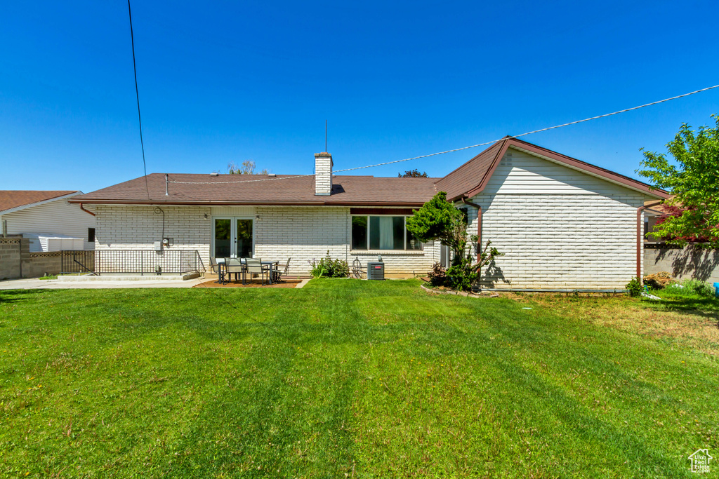 Rear view of house with brick siding, a chimney, a patio area, cooling unit, and french doors