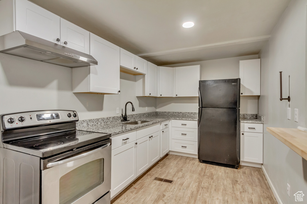 Kitchen featuring freestanding refrigerator, electric range, a sink, under cabinet range hood, and light wood-style flooring