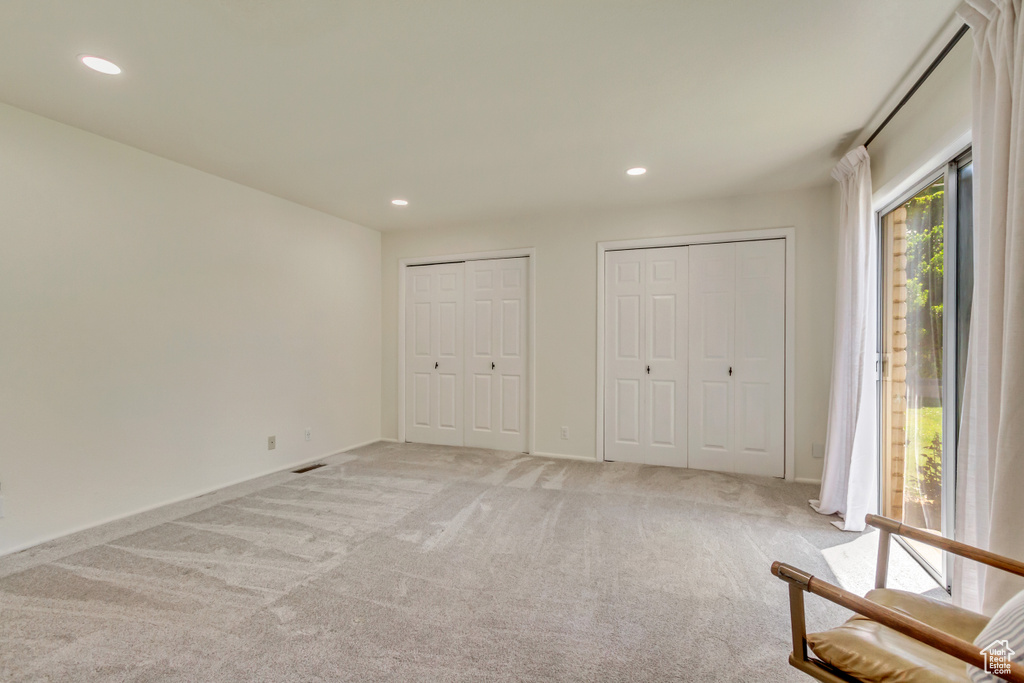Unfurnished bedroom with light colored carpet, two closets, recessed lighting, access to exterior, and baseboards
