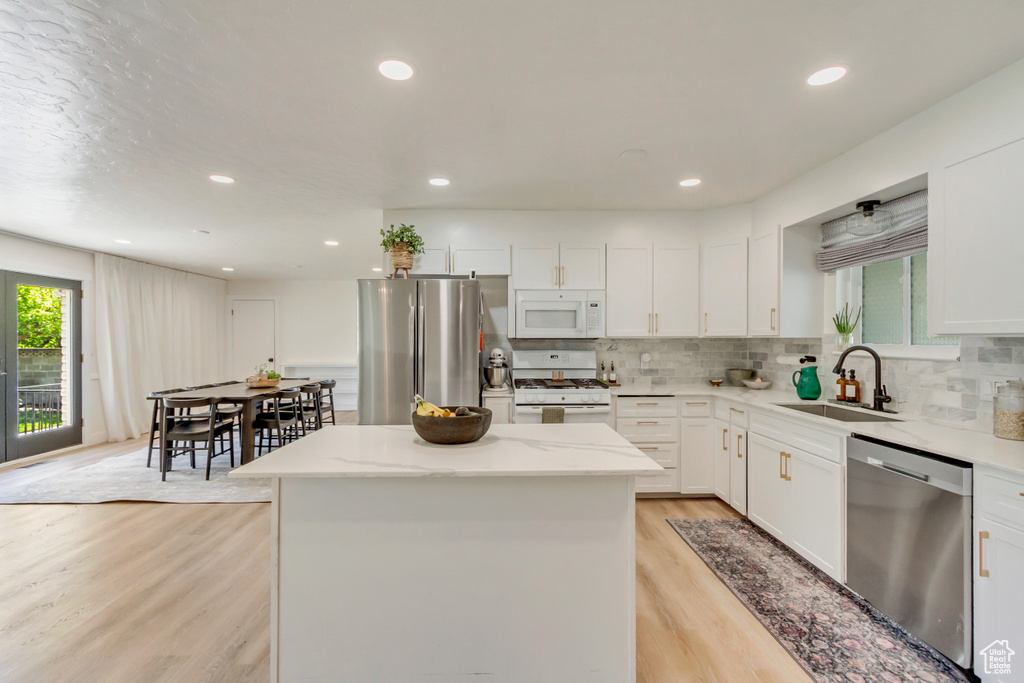 Kitchen featuring appliances with stainless steel finishes, a sink, light wood-style flooring, a center island, and decorative backsplash