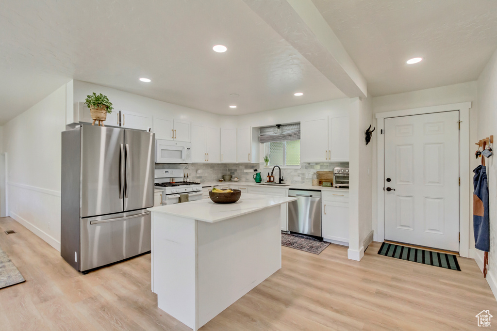 Kitchen featuring stainless steel appliances, white cabinets, light wood finished floors, decorative backsplash, and recessed lighting