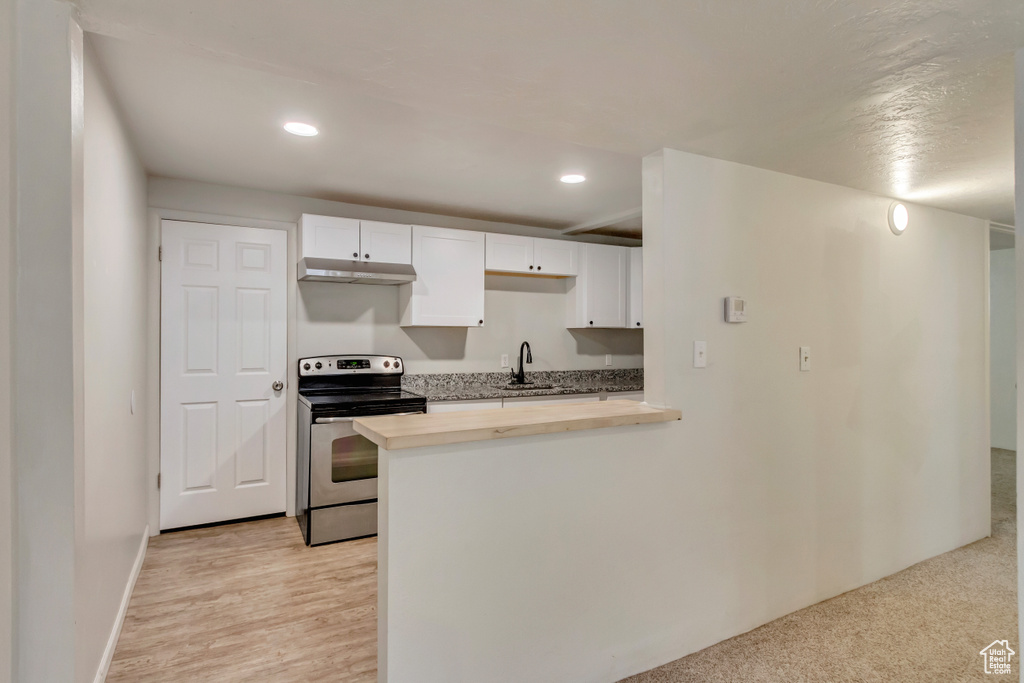 Kitchen with stainless steel electric range oven, butcher block countertops, a sink, recessed lighting, and white cabinets