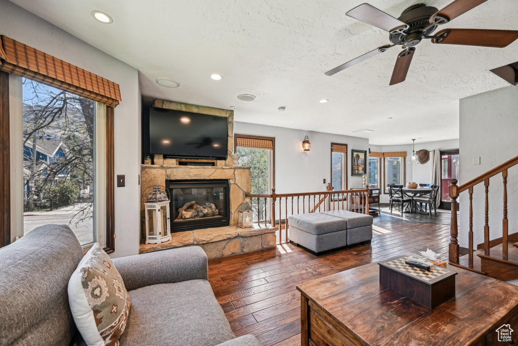 Living room with hardwood / wood-style floors, ceiling fan, a stone fireplace, a textured ceiling, and recessed lighting
