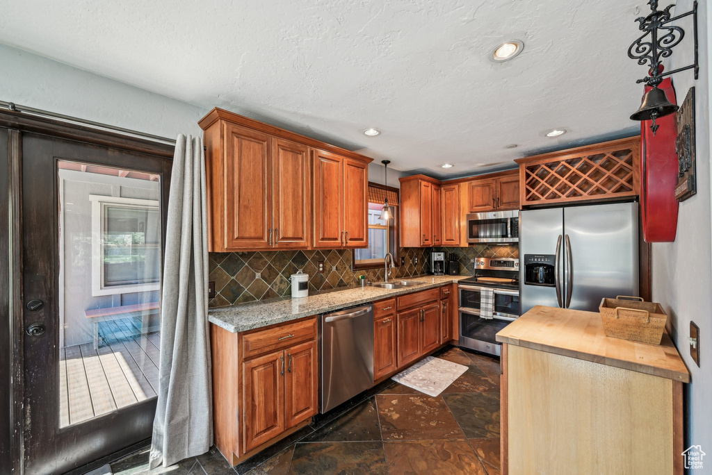 Kitchen with appliances with stainless steel finishes, a sink, backsplash, brown cabinets, and recessed lighting