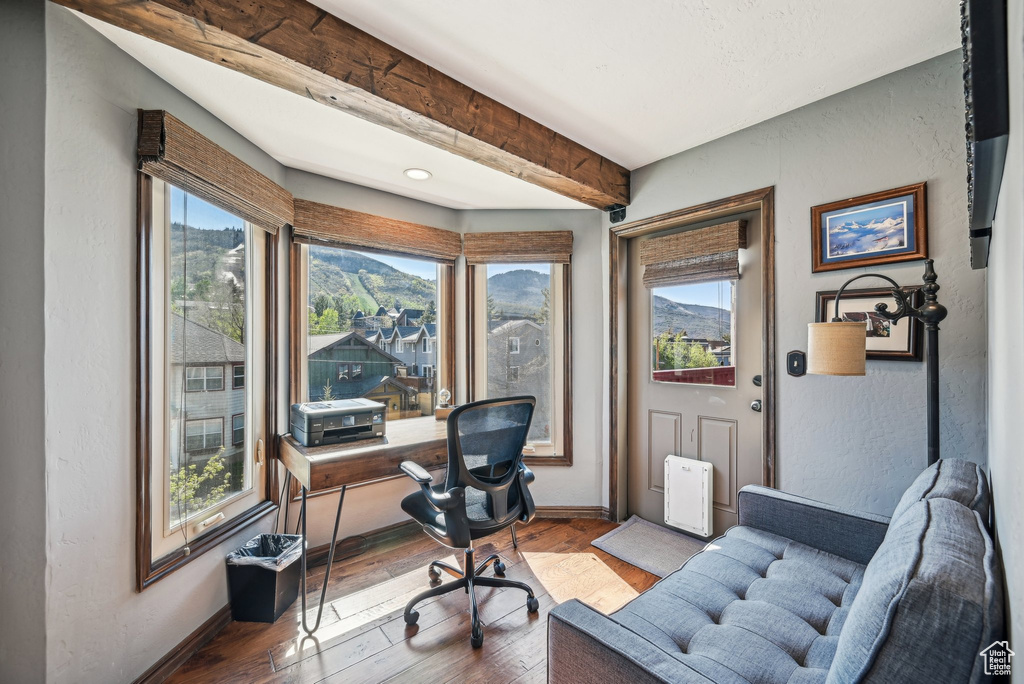 Office space featuring baseboards, hardwood / wood-style flooring, beam ceiling, and a textured wall