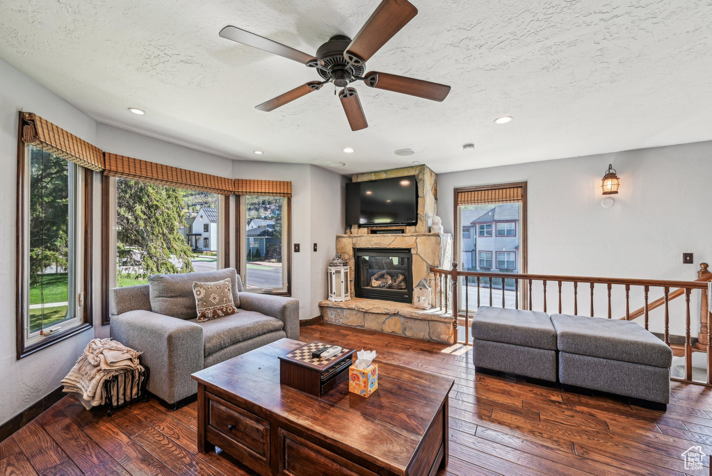Living area featuring a textured ceiling, a stone fireplace, a ceiling fan, dark wood-style flooring, and recessed lighting