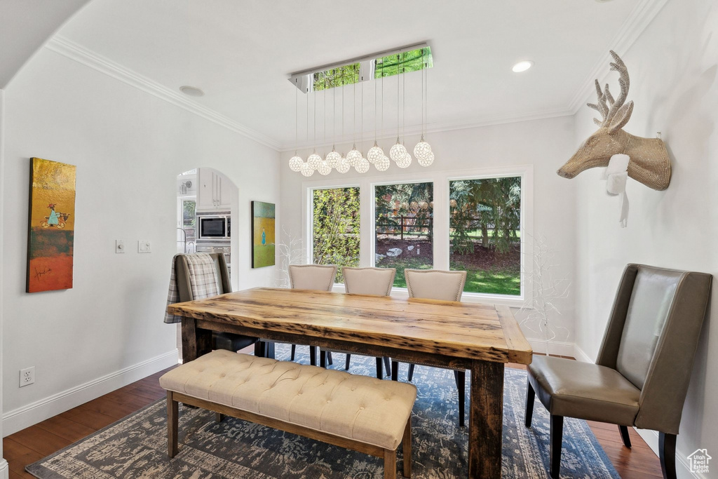 Dining room featuring arched walkways, baseboards, dark wood-type flooring, ornamental molding, and recessed lighting