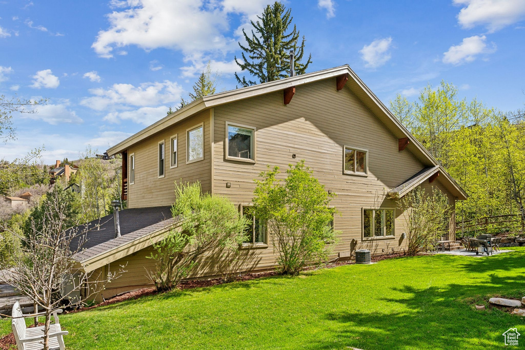 Back of property with central AC unit, a lawn, and a patio