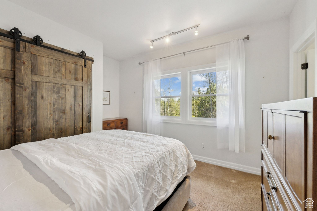 Bedroom with light colored carpet, a barn door, and baseboards
