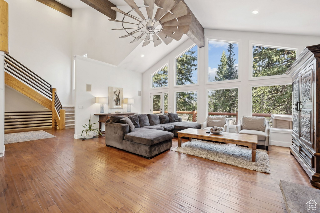 Living room with beamed ceiling, plenty of natural light, high vaulted ceiling, stairs, and wood-type flooring