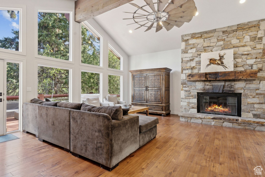 Living area with high vaulted ceiling, a stone fireplace, hardwood / wood-style floors, beam ceiling, and a ceiling fan