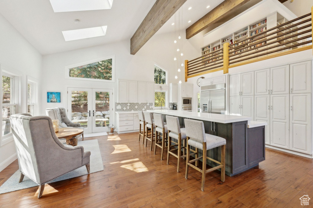 Kitchen featuring built in appliances, high vaulted ceiling, white cabinets, a large island, and decorative backsplash
