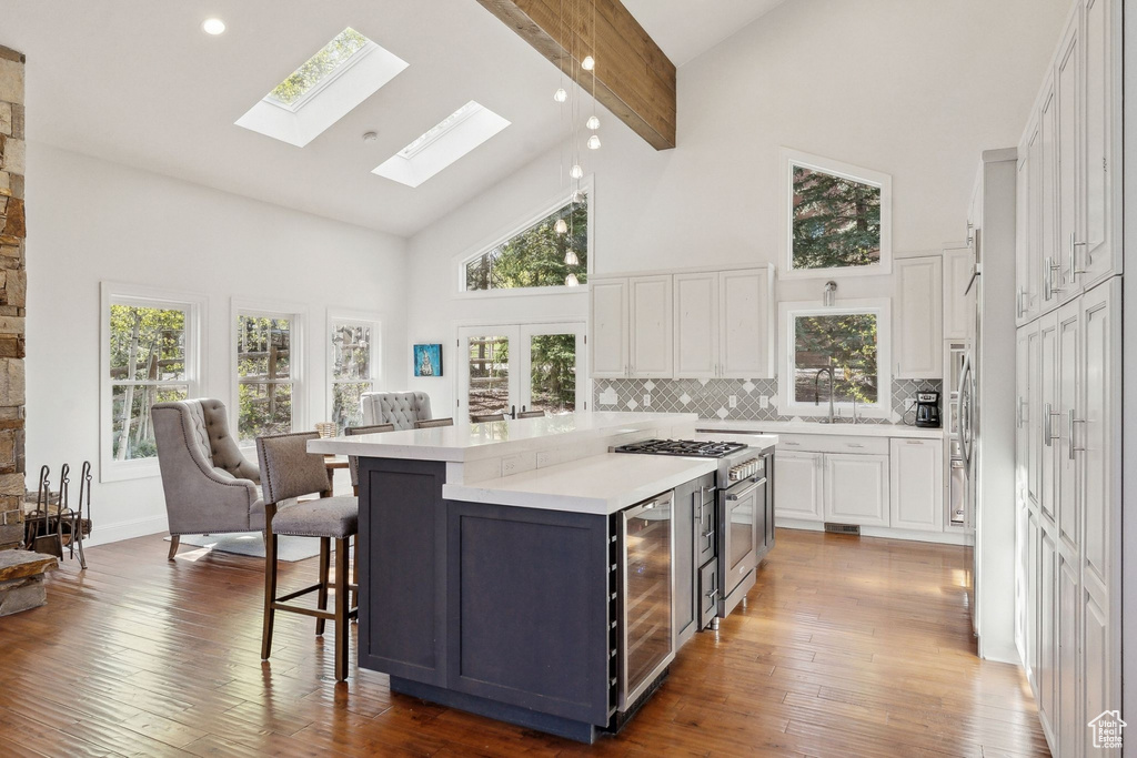Kitchen with high vaulted ceiling, beverage cooler, white cabinets, light countertops, and decorative backsplash