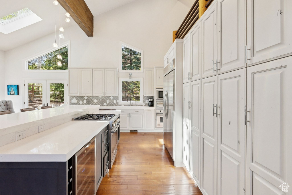 Kitchen with wine cooler, high vaulted ceiling, light wood-style floors, white cabinetry, and a skylight