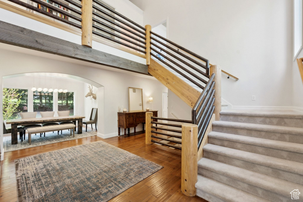Stairs with arched walkways, wood finished floors, a towering ceiling, and baseboards