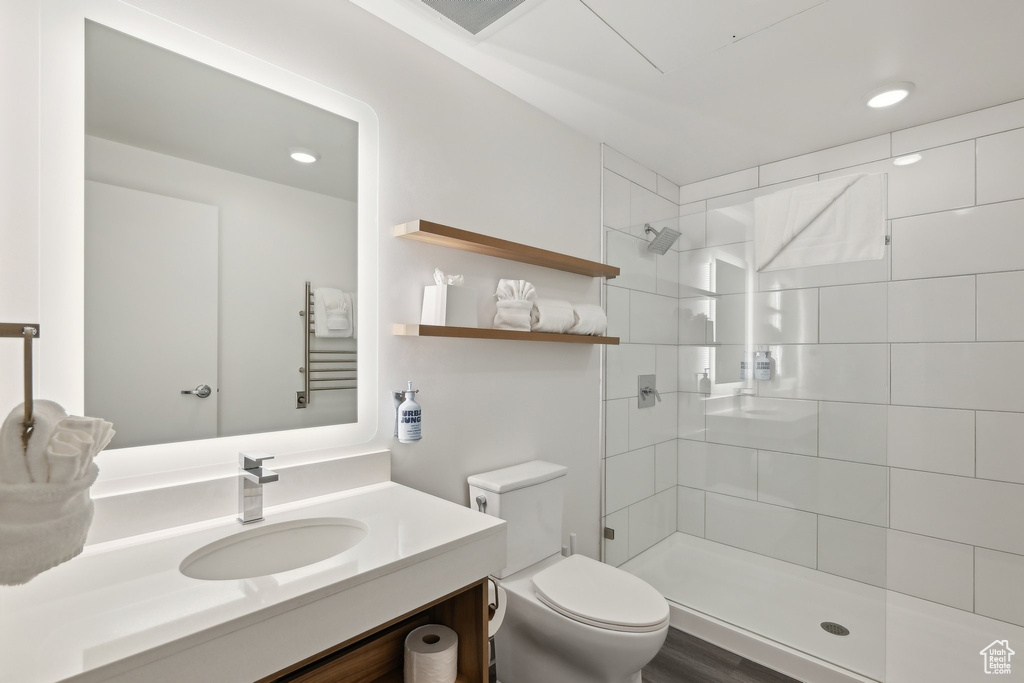 Full bathroom with toilet, a tile shower, vanity, a towel warming rack, and recessed lighting